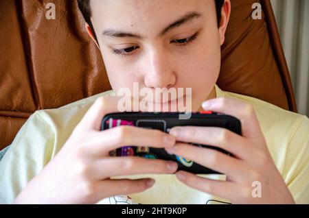 Ein Junge konzentriert sich, während er ein Spiel auf einem Mobiltelefon spielt. Stockfoto