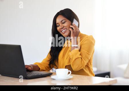 Arbeiten als eigener Chef. Aufnahme einer fröhlichen jungen Geschäftsfrau, die zu Hause am Laptop arbeitet und mit ihrem Handy spricht. Stockfoto