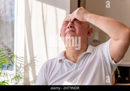 Ein gereifter älterer Mann zu Hause kneift und reibt seinen Kopf, fühlt sich unwohl und oder hat Schmerzen. Gefühl Unwohlsein Konzept. Stockfoto