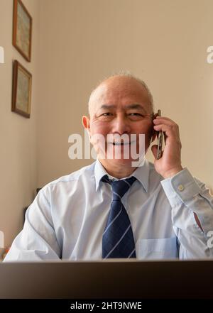 Ein gereifter leitender Büroangestellter mit einem großen Lächeln, nachdem er am Telefon gute Nachrichten über ein großes Geschäft gehört hat. Stockfoto