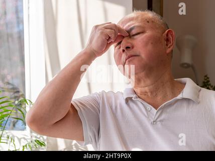 Ein gereifter älterer Mann zu Hause kneift und reibt seinen Kopf, fühlt sich unwohl und oder hat Schmerzen. Gefühl Unwohlsein Konzept. Stockfoto
