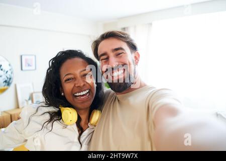 Fröhliches Selfie zu Hause gemischtes Rennpaar lächelt und schaut in die Kamera. Glücklicher Mann und schöne Frau, die selbst fotografieren und Spaß haben Stockfoto