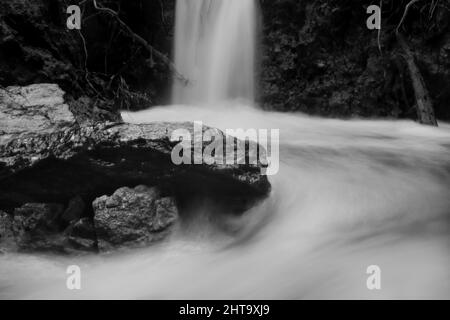 Graustufenaufnahme des Wassers, das flussabwärts auf einem felsigen Wasserfall fließt, mit langer Belichtung Stockfoto