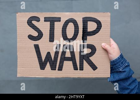 Nahaufnahme der Hand einer Person, die ein handgemachtes Banner mit dem „Stop war“-Slogan auf grauem Hintergrund hält. Stockfoto