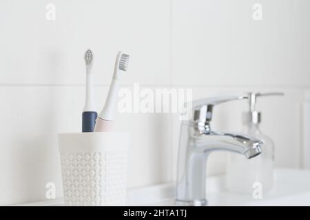 Neue moderne Ultraschall-Zahnbürsten in einem Glas auf dem Waschbecken. Kiefer Modell und zahnärztliche Versorgung liefert. Mundhygiene, Zahn- und Zahnfleischgesundheit, gesund Stockfoto