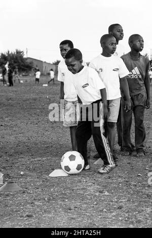 Graustufen-Aufnahme von jungen afrikanischen Kindern, die auf einem Schulhof Fußballaktivitäten durchführen Stockfoto