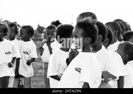 Graustufen-Aufnahme von jungen afrikanischen Kindern, die auf einem Schulhof Fußballaktivitäten durchführen Stockfoto