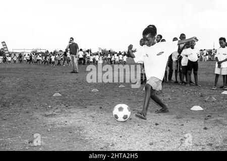 Graustufen-Aufnahme von jungen afrikanischen Kindern, die auf einem Schulhof Fußballaktivitäten durchführen Stockfoto