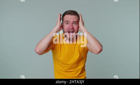 Bärtiger erwachsener Mann hat Angst, Ohren mit Händen bedeckt, Augen geschlossen, seine eigene Phobie erfüllt, ein Horrorereignis bezeugt, schreiend, laut schreiend, Stockfoto