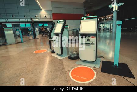 Eine Seitenansicht der elektronischen Check-in-Automaten in einem modernen Flughafen mit einem Modell ihrer LCD-Bildschirme; ein Desinfektionsstand in der Nähe und so Stockfoto