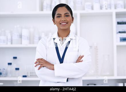 Ich bin zuversichtlich in meine wissenschaftlichen Fähigkeiten. Beschnittenes Porträt einer attraktiven jungen Wissenschaftlerin, die mit gefalteten Armen im Labor steht. Stockfoto