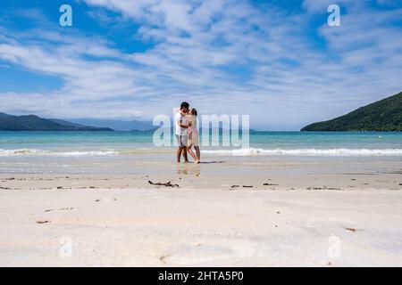 Das lateinische Paar küsst sich an einem paradiesischen Strand mit weißem Sand und blauem Meer auf der Insel Anchieta in Brasilien. Stockfoto
