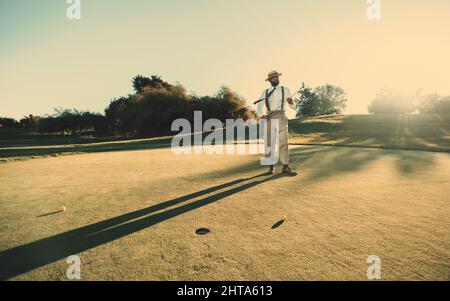 Weite Fernansicht eines hübschen kahlen schwarzen Golfspielers, der auf dem grünen Gras eines Golffeldes steht und seinen Schläger hält. Ein reifer Mann mit einem Golf st Stockfoto