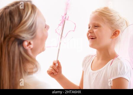 Ich mache Ihren Wunsch wahr. Ein lächelndes Mädchen, das sich als Fee verkleidet und einen Zauberstab vor ihrer Mutter hält. Stockfoto