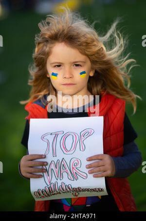 Kind Junge hält Schild mit Worten Stoppt den Krieg im Freien stehen. Kind trägt ein Schild Krieg stoppen. Putin greift das ukrainische Volk an. Stockfoto