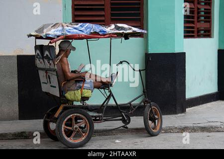 Ein Mann, der in seinem Fahrradtaxi in Havanna, Kuba, ein Buch liest. Stockfoto