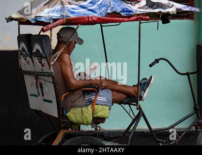 Ein Mann, der in seinem Fahrradtaxi in Havanna, Kuba, ein Buch liest. Stockfoto