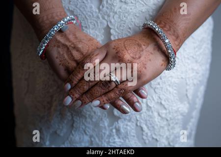 Nahaufnahme der Hände einer südasiatischen Braut, bedeckt mit wunderschönem Henna und Schmuck Stockfoto