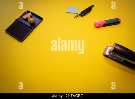 Eine Draufsicht auf einen Holzstempel mit Tinte, Metallhefter, Haftnotizen und Markern isoliert auf gelbem Hintergrund Stockfoto