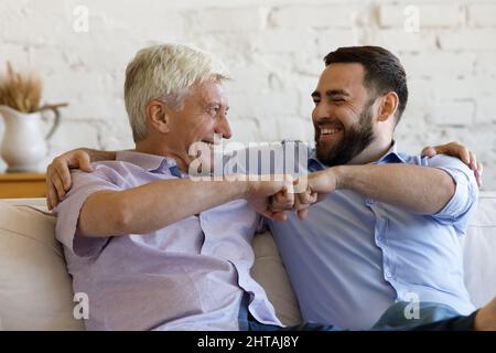 Glücklicher älterer Mann, sein Sohn, auf dem Sofa sitzend, hat eine Faust gebumt Stockfoto