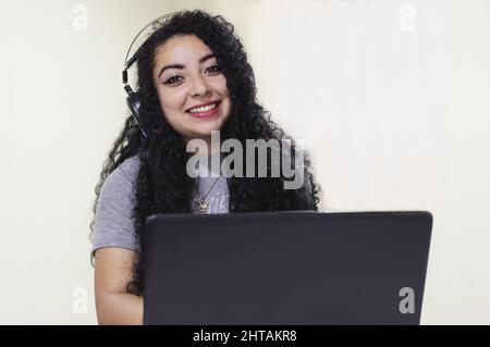 Nahaufnahme einer hispanischen Frau, die an ihrem Laptop arbeitet, während sie Kopfhörer trägt Stockfoto