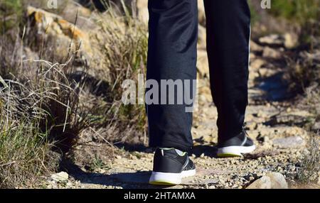 Rückansicht eines Mannes mit schwarzen Schuhen, der auf einer unbefestigten Straße unterwegs ist Stockfoto