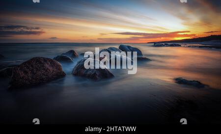 Atemberaubende Aussicht auf den Sonnenaufgang am Meer mit großen Steinen, die von Morgennebel bedeckt sind Stockfoto