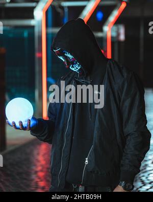 Mann in einer blauen Neonmaske, der den Mond als Zauberer hält Stockfoto