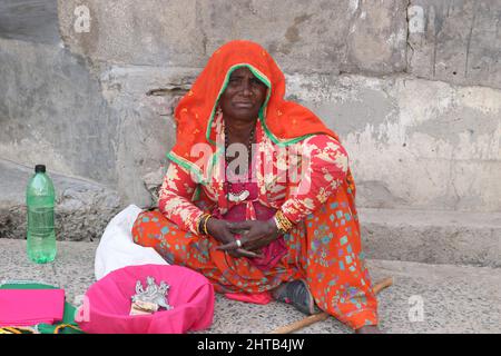 Eine Bettlerin, die in farbenfrohem Kleid auf der Straße sitzt. Stockfoto