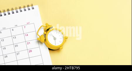 Gelber Wecker und Kalender auf gelbem Hintergrund. Vorlage Kopierraum für Text. Modell. Stockfoto