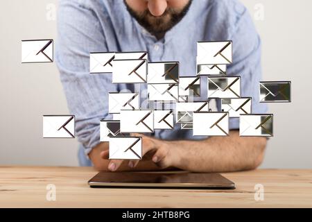 3D Rendering von silbernen E-Mail-Symbolen, die in der Luft schweben, mit einem Mann, der unter ihnen ein Tablet ansieht Stockfoto
