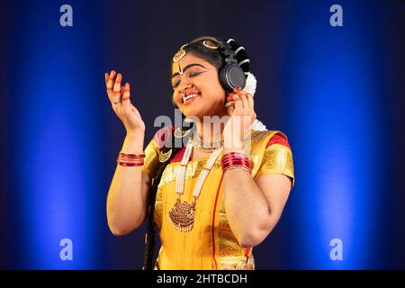 Genießen Sie die indische bharatanatyam-Tänzerin, indem Sie auf der Bühne Songs über Kopfhörer hören - Konzept der Entspannung, Stressabbau und Unterhaltung. Stockfoto