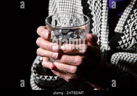 Porträt einer älteren Frau mit einem Glas Wasser auf schwarzem Hintergrund Stockfoto