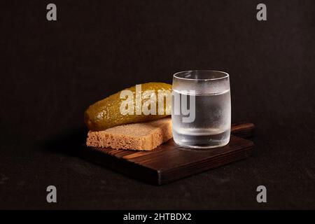 Ein Glas Wodka, Roggenbrot und eine Gurke auf einem Holzständer Stockfoto