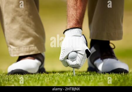 Einrichten. Zugeschnittenes Bild eines Golfspielers, der seinen Golfball auf das T-Shirt legt. Stockfoto