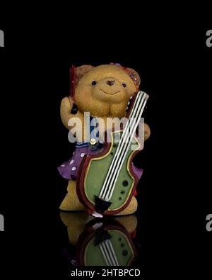Vertikale Aufnahme einer alten, kleinen, farbenfrohen Bärenstatue mit einer Gitarre auf schwarzem Hintergrund Stockfoto