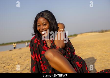 Eine attraktive junge afrikanische Frau, die lächelt und am Strand posiert Stockfoto