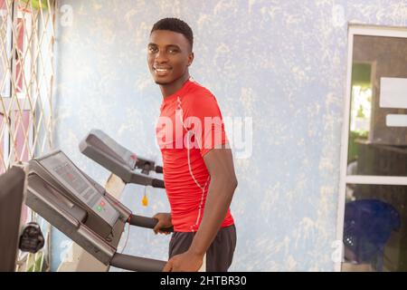 Junger, sportlicher afrikanischer Mann, der in einem Fitnessstudio auf einem Laufband läuft Stockfoto