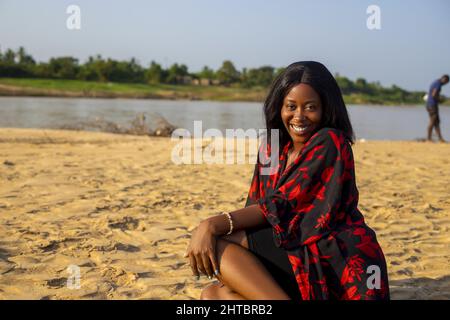 Attraktive junge afrikanische Frau, die lächelt und am Strand posiert Stockfoto