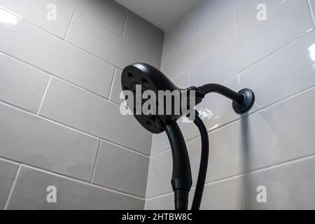 Nahaufnahme eines modernen abnehmbaren schwarzen Duschkopfes in einer weiß gefliesten Badewanne Stockfoto