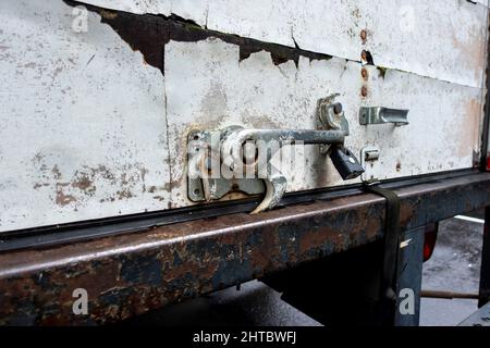 Abgewinkelte Nahaufnahme einer verrosteten Metallverriegelung auf der Rückseite eines weißen fahrenden Lkw mit einer schwarzen Trittleiter Stockfoto