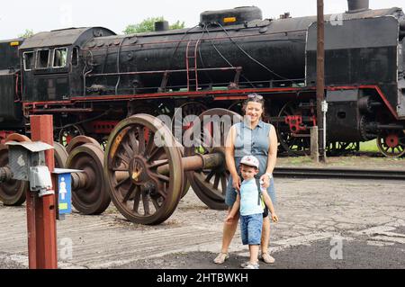 Frau und Kind stehen vor einer alten Ausstellungslokomotive in einem Freilichtmuseum Stockfoto