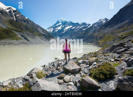 Eine kaukasische Frau, die auf die Entfernung zum Hooker Valley schaut, das zum Aoraki Mount Cook in Neuseeland führt Stockfoto