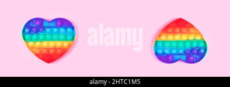 Banner aus Pop it Anti-Stress-Spielzeug in Form von Herz isoliert auf rosa Hintergrund. Nahaufnahme. Stockfoto