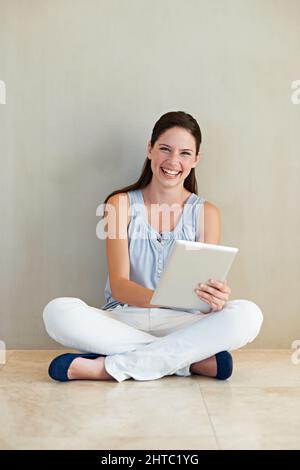 Das ist so einfach zu bedienen. Eine schöne junge Frau, die ihr Tablet benutzt, während sie auf dem Boden sitzt. Stockfoto
