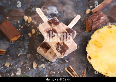 Nahaufnahme von hausgemachten Eiszapfen mit verschiedenen Geschmacksrichtungen über schwarzem Tisch mit Früchten und Schokolade Stockfoto