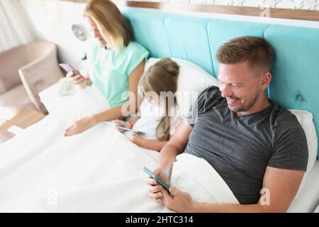 Familie starren im Smartphone, morgens im Bett mit Geräten, Kill Time Stockfoto