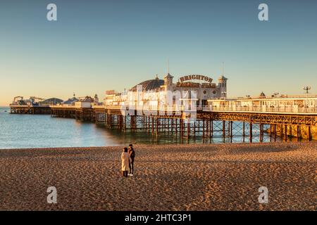 14. Januar 2022: Brighton, East Sussex, Großbritannien - Sonnenaufgang am Brighton Palace Pier, mit einem jungen Paar am Strand. Stockfoto