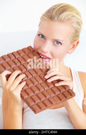 Ich esse nur ein wenig davon Junge Frau beißt in eine riesige Tafel Schokolade. Stockfoto