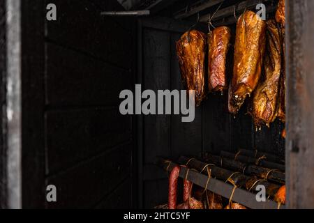 Nahaufnahme von geräuchertem Fleisch und Bauch- oder Buchenfleisch mit dunkler Kruste in der Räucherei oder Raucher, Food-Konzept Stockfoto